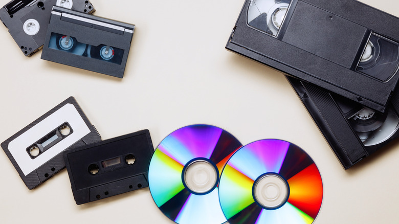 An assortment of cassettes, CDs, and VHS tapes against an off-white background.