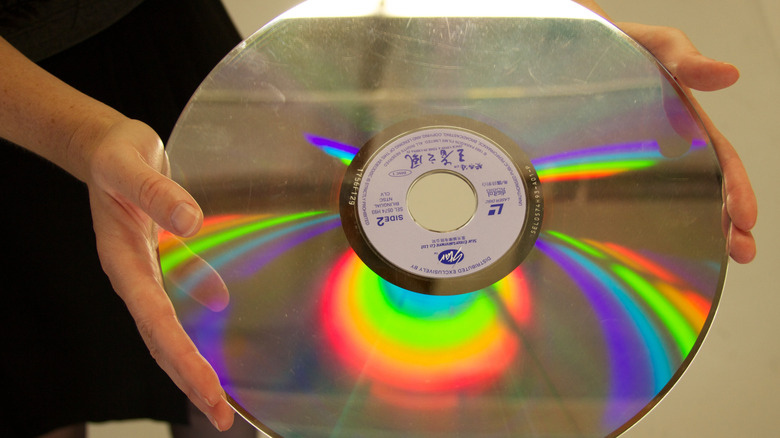 A pair of hands holding a Taiwanese LaserDisc with a rainbow reflection on it.