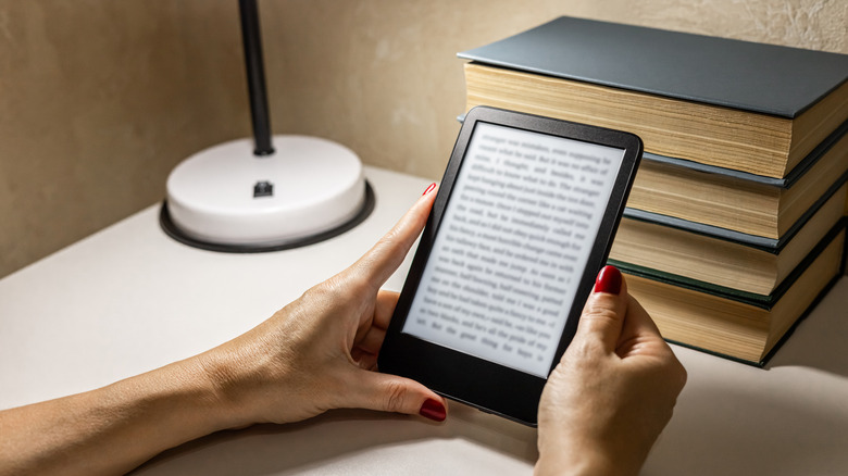 A woman reads an e-reader by the light of a table lamp.