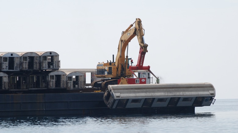 Construction vehicle dumping MTA subway train into ocean.