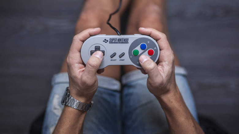 Person holding a Super Nintendo Entertainment System controller while playing a game