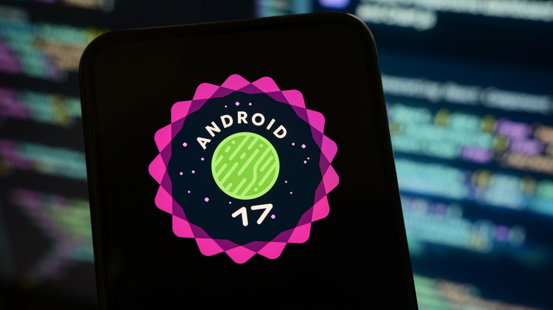 A smartphone screen showing the logo for Android 17 with a blurred computer screen in the background