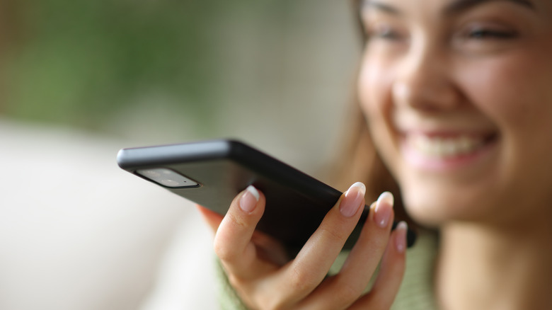 A smiling woman using her phone to dictate a message.