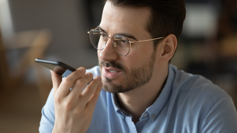 A bespectacled man speaks into a smartphone.