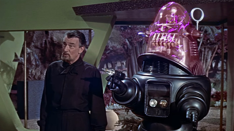 Doctor Morbius stands besides his robot Robby, who, holding a fun, malfunctions.