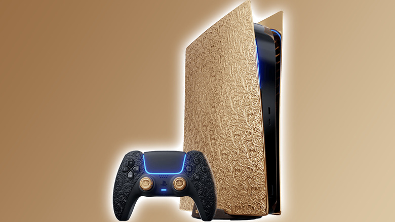 A PlayStation 5 with gold side panels covered in an ornate engraved floral pattern, next to a black DualSense controller with an embossed floral texture.