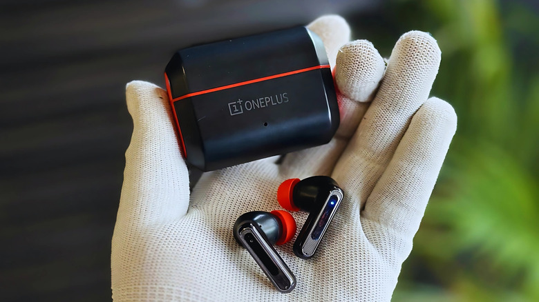 Close-up of a gloved hand holding OnePlus earbuds in a charging case
