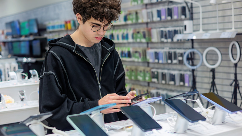 A young person looking at smartphones in an electronics strore.
