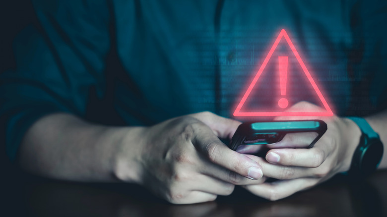 A red scam icon projects from a phone screen as a faceless man types.