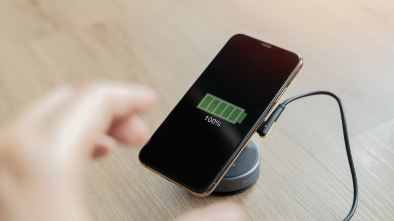 Smartphone on a charger, showing 100% battery.