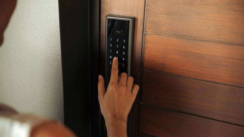 Person entering a code on a smart lock mounted on a wooden door.