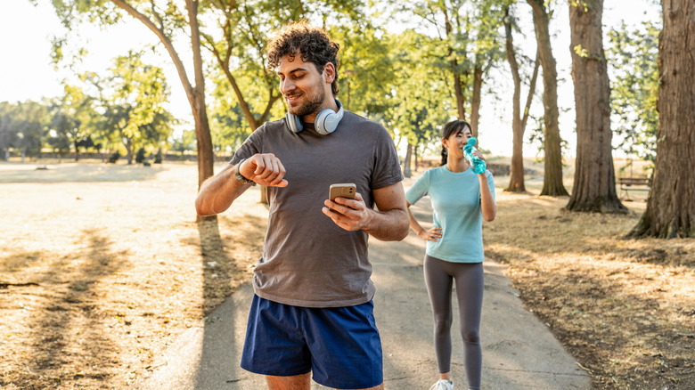 A couple out on a run through the park with the man looking at his smartwatch.