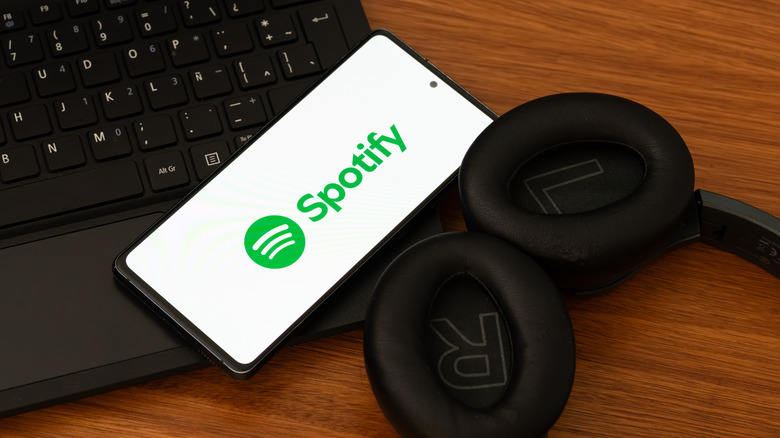 Smartphone featuring Spotify logo next to laptop and headphones