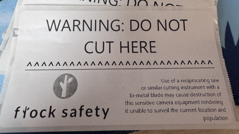 Anti-Flock activists create facetious DO NOT CUT HERE posters warning citizens that destroying Flock cameras may render it "unable to surveil the current location and population"