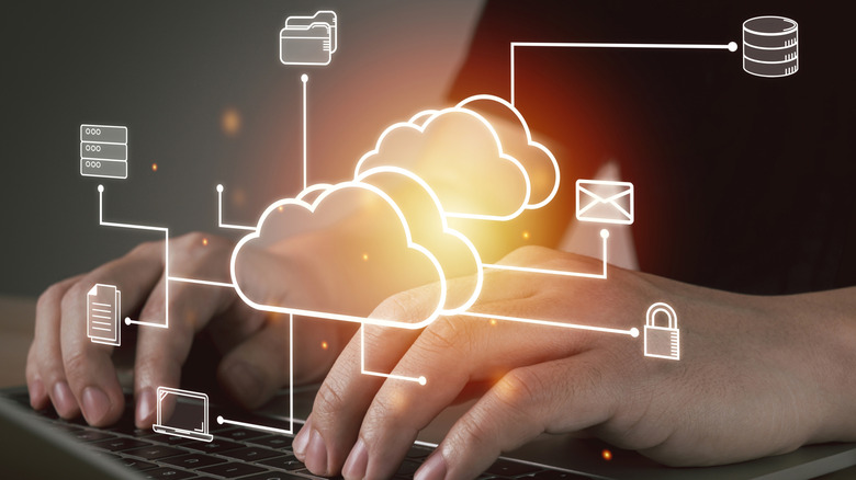 Fingers type at a laptop with cloud imagery in the foreground