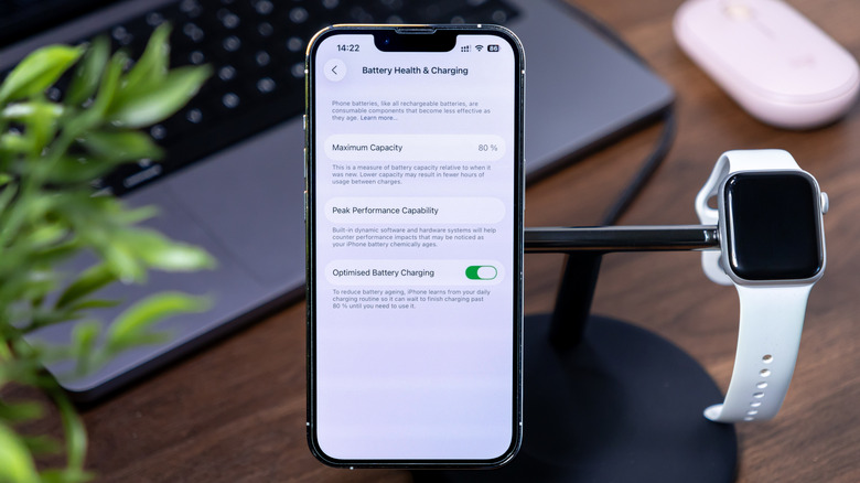 An iPhone on a charging stand showing the Battery Health page with an Apple Watch charging alongside