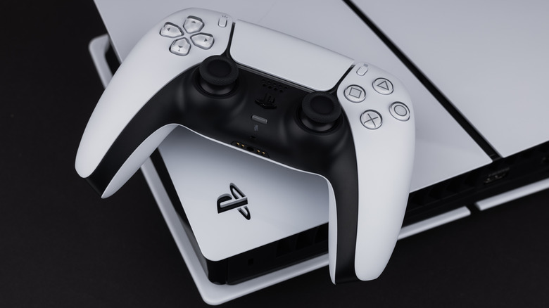 A white DualSense PS5 controller sits on a white PS5 against a black background