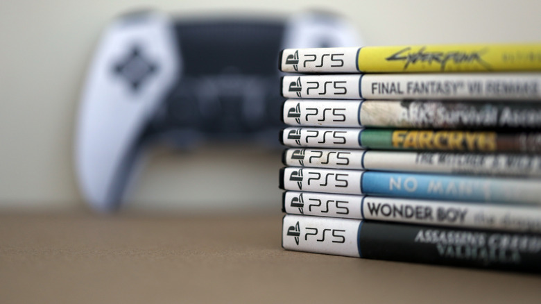 Pile of PlayStation 5 disc cases in front of DualSense controller
