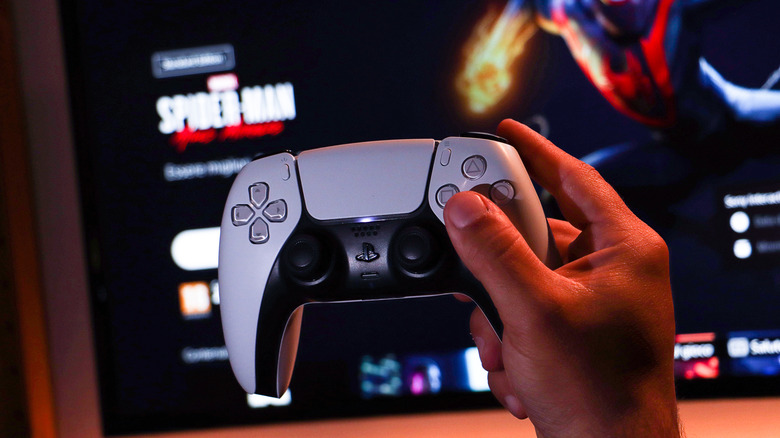 Player holding DualSense PlayStation 5 controller in front of TV with Spider-Man in background.