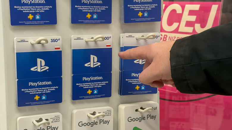 Person pointing at PlayStation physical gift cards on a store rack.