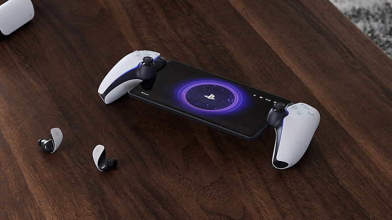 A PlayStation Portal handheld gaming device beside wireless earbuds on a wooden surface.
