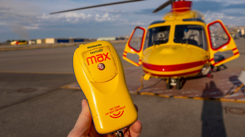a hand holding a PLB with a rescue helicopter nearby