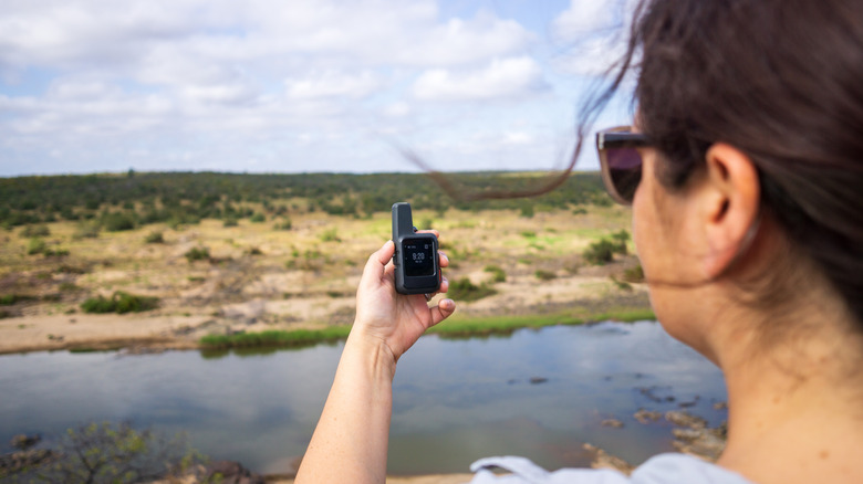a woman holding a satellite messenger out in the wilderness