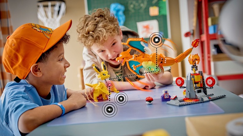 Two children playing with a Lego Pokemon Smart Play set featuring Charizard and Jolteon