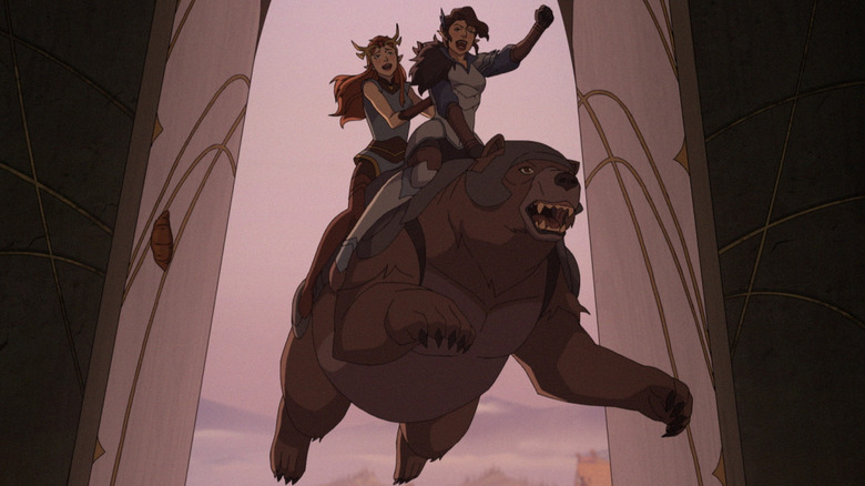 Keyleth and Vex riding on the back of Trinket, a large brown bear wearing armor