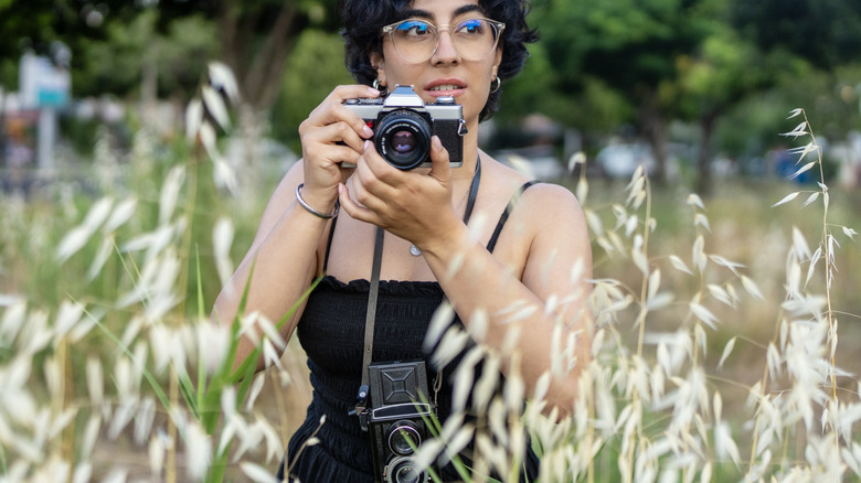 A photographer using a film camera while a classic model hangs from her neck.