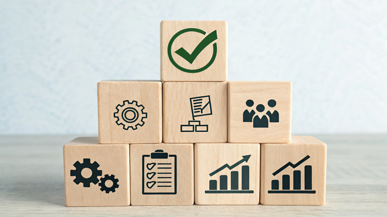 Wooden blocks stacked with icons on them representing teamwork, cogs, and checklists