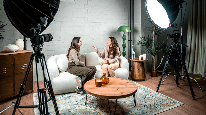 Two podcast participant sitting on a couch under studio lights during recording