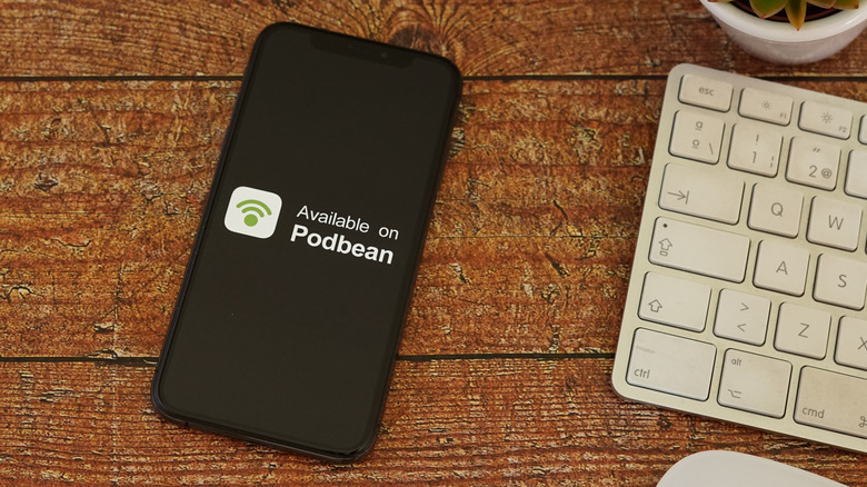 The Podbean logo and slogan on a smartphone next to a keyboard