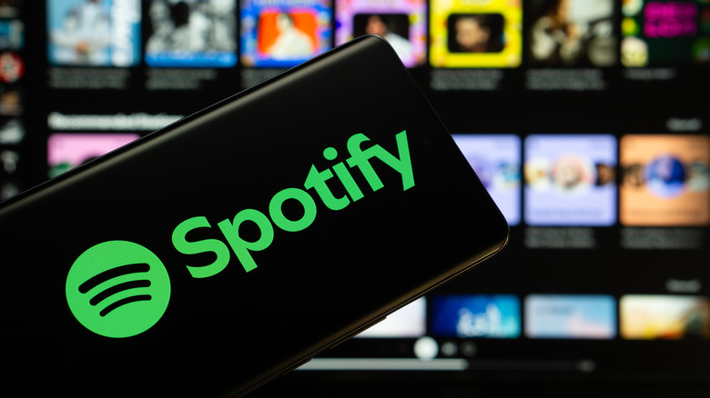 The Spotify logo on a smartphone screen against a blurry grid of other screens