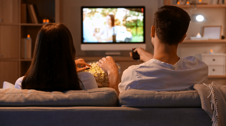 Couple sitting in front of TV eating popcorn