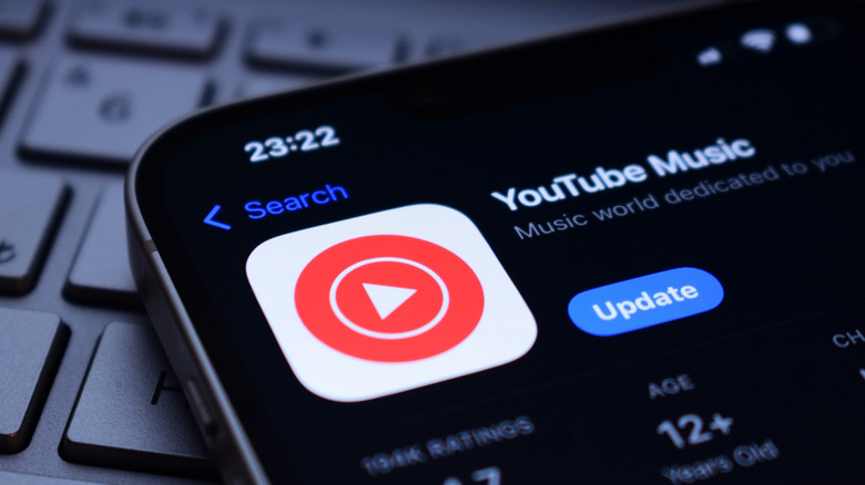 A close-up of a smartphone laying on a keyboard with the YouTube Music app icon on the screen