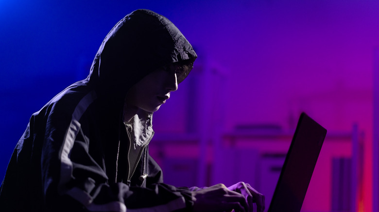Sinister-looking person in a hoodie working on a laptop