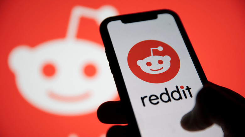 phone showing reddit logo on white background, hand visible