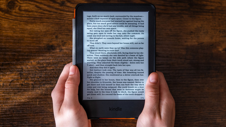 Hands holding Kindle e-reader displaying ebook page on wooden surface