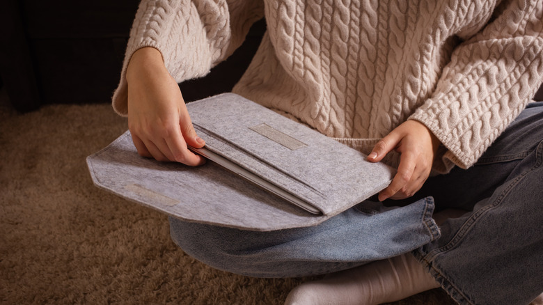 Person placing MacBook inside a soft sleeve case while sitting on a floor.