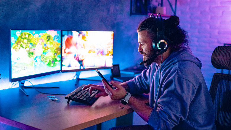 A person in front of their PC setup using their phone with headphones on