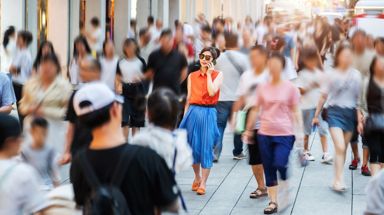 woman walking on sidewalk in crowd of people while talking on phone