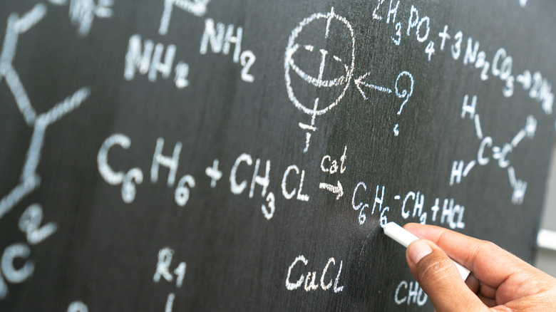 hand writing on chalkboard with various physics-based symbols and equations