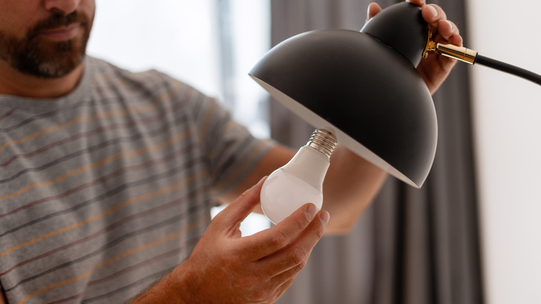 A man installing an LED light bulb in a black lamp
