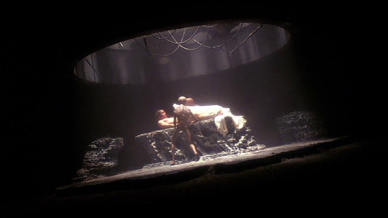 Two aliens doing tests on Travis in their spaceship