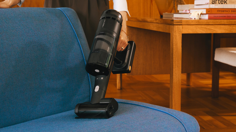 A woman cleans her sofa with the Roborock H60 Hub Ultra with a mini brush installed
