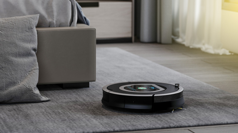 A robot vacuum cleaning a gray carpet in a bedroom