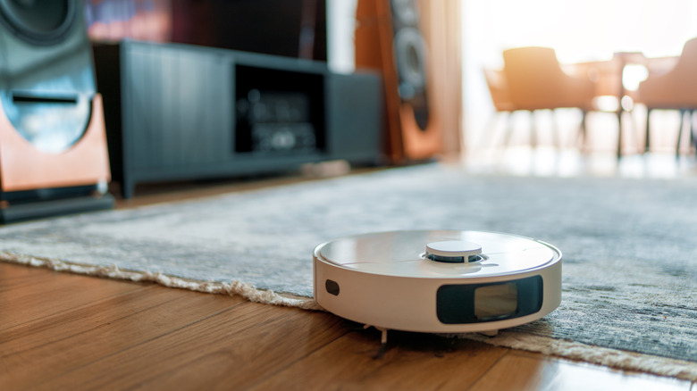 A robot vacuum cleaning a rug in a room with a large stereo