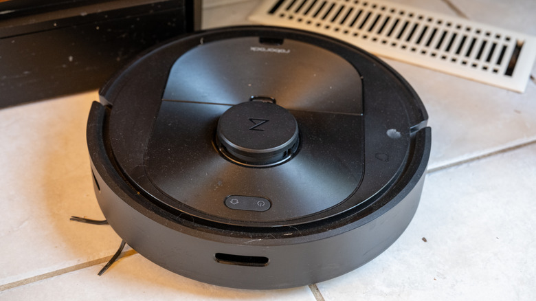 A black robot vacuum cleaning a white tile floor