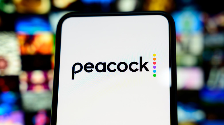 The Peacock logo is on the display of a cellphone in front of an incredibly blurred background